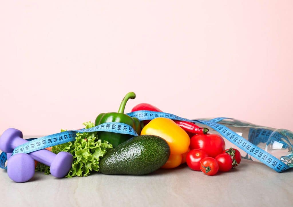How to Lose Weight Without Exercise 16 An assortment of colourful fruits and vegetables displayed alongside a measuring tape, representing dietary measurement.