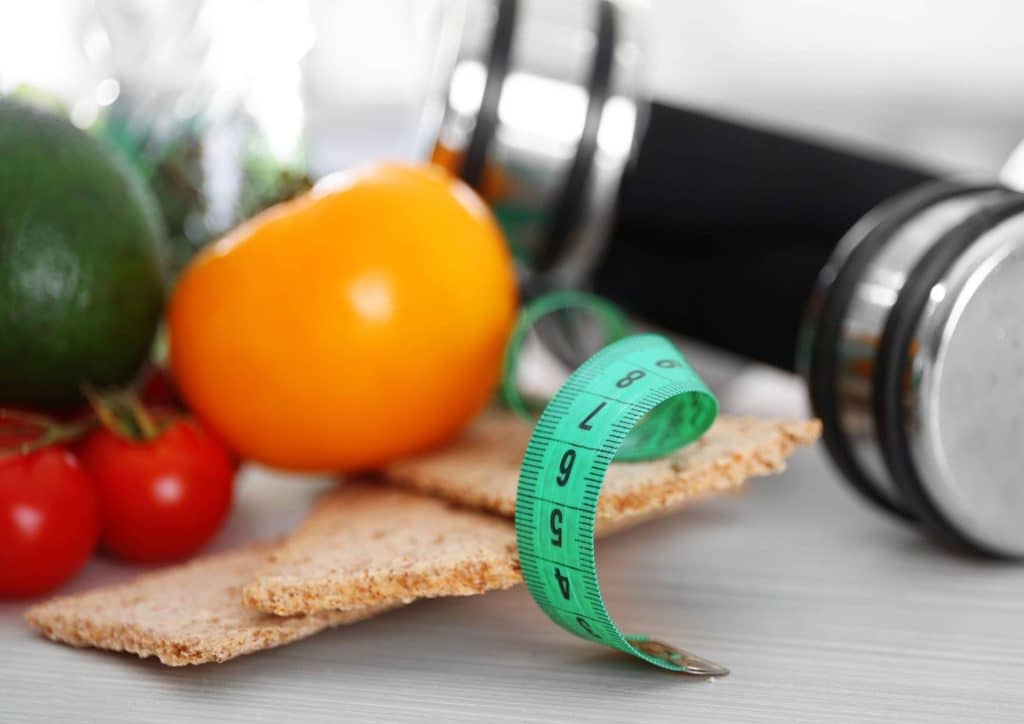 How to Lose Weight Without Exercise 14 A scale and measuring tape placed beside a variety of fresh vegetables on a wooden surface.