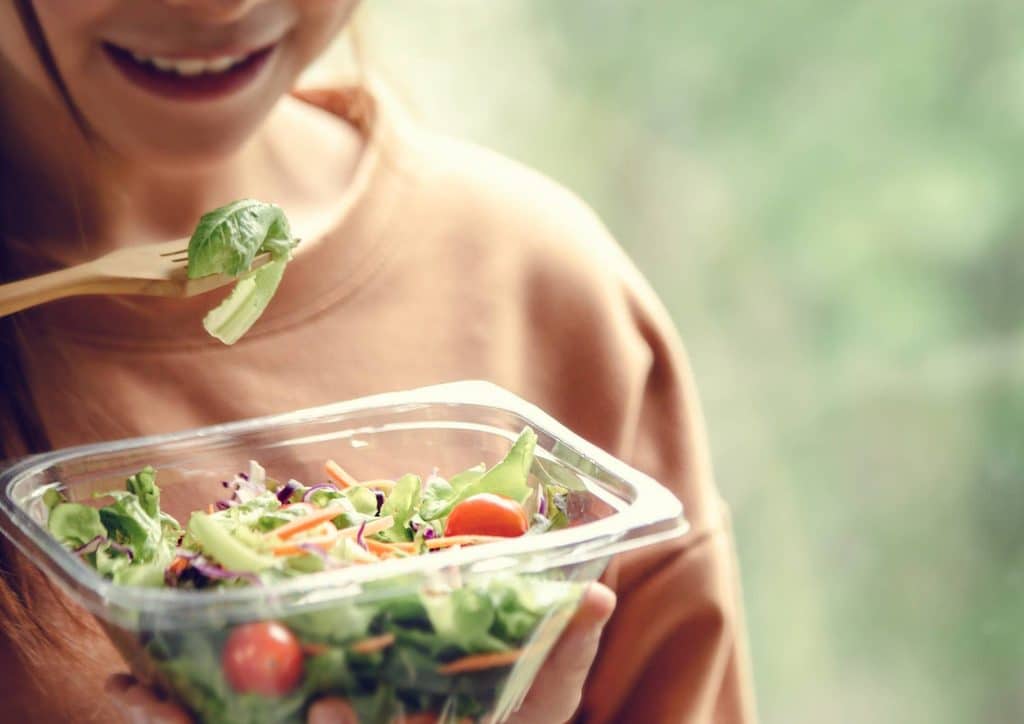 Natural Alternatives to Ozempic for Weight Loss 16 A woman holds a plastic container filled with a colourful salad, smiling as she prepares to enjoy her meal.