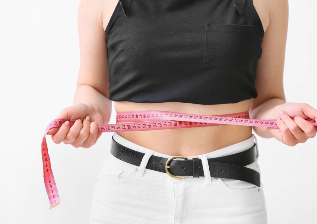 Natural Alternatives to Ozempic for Weight Loss 3 A woman in a black top and white jeans holds a measuring tape, appearing focused on a measurement task.