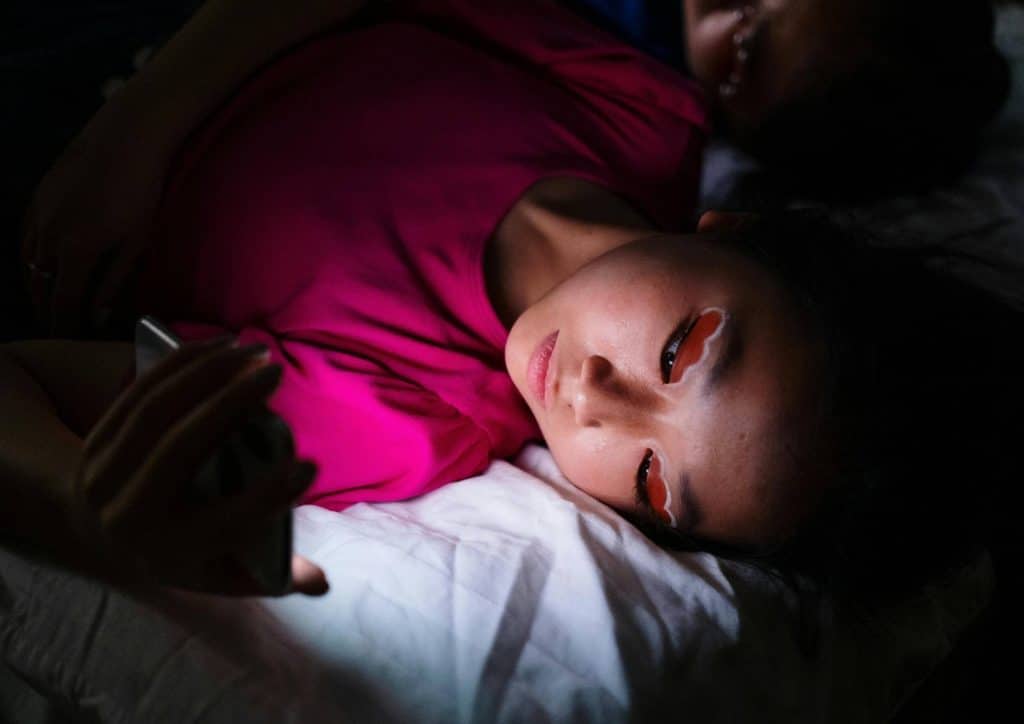 Why Am I Not Losing Weight? 8 Reasons a Nutritionist Sees Every Week 13 A woman lies in bed with her eyes closed, holding a cell phone beside her.