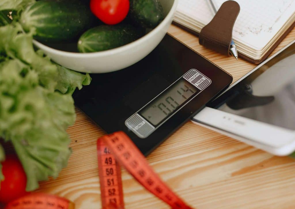 Not Losing Weight in a Calorie Deficit? Here's Why 9 Digital scale next to a bowl of fresh vegetables and a smartphone, indicating a healthy meal preparation setup.