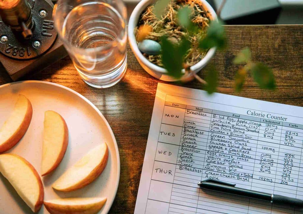 Not Losing Weight in a Calorie Deficit? Here's Why 25 A plate of red apples, a steaming cup of coffee, and a pen arranged on a wooden table.
