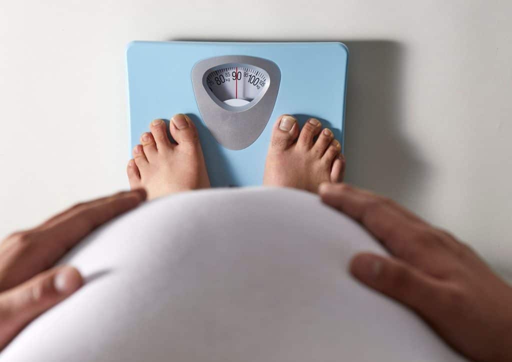 How to Lose Weight Without Exercise 23 Pregnant woman's feet positioned on a scale, indicating weight measurement during pregnancy.