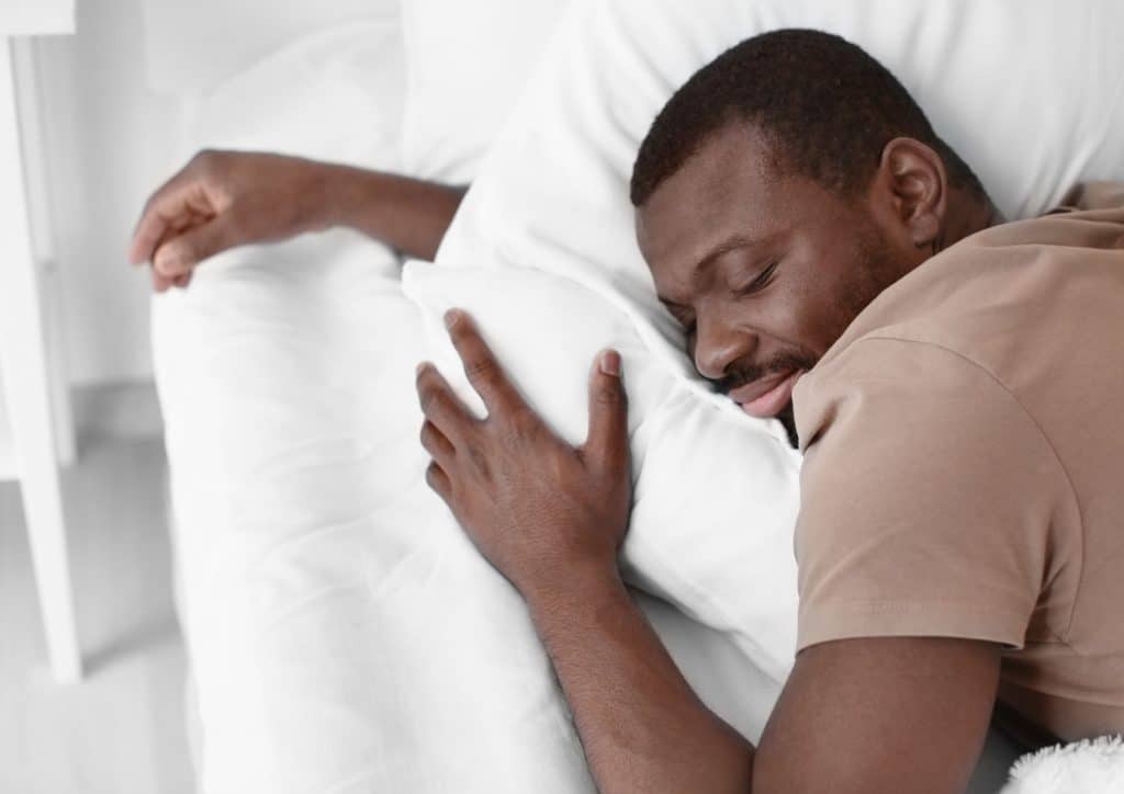 Natural Alternatives to Ozempic for Weight Loss 19 A man peacefully sleeping in bed with his eyes closed, surrounded by soft bedding and pillows.