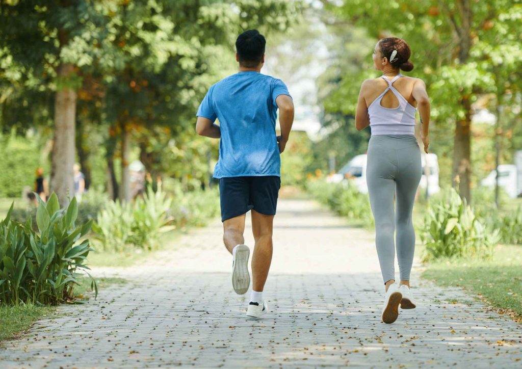 Natural Alternatives to Ozempic for Weight Loss 21 A man and woman jogging together on a path in a green park, surrounded by trees and sunlight.