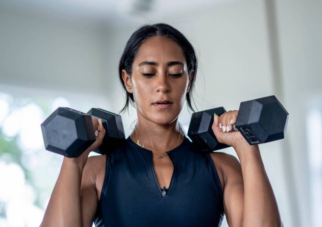 Natural Alternatives to Ozempic for Weight Loss 22 A woman performs a strength training exercise, lifting two dumbbells in a gym setting.