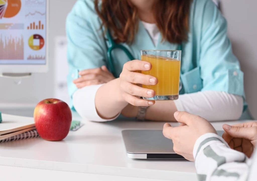 How to Choose the Best Weight Loss Nutritionist in Sydney 16 A woman sitting at a desk holds a glass of juice, appearing focused and engaged in her work environment.