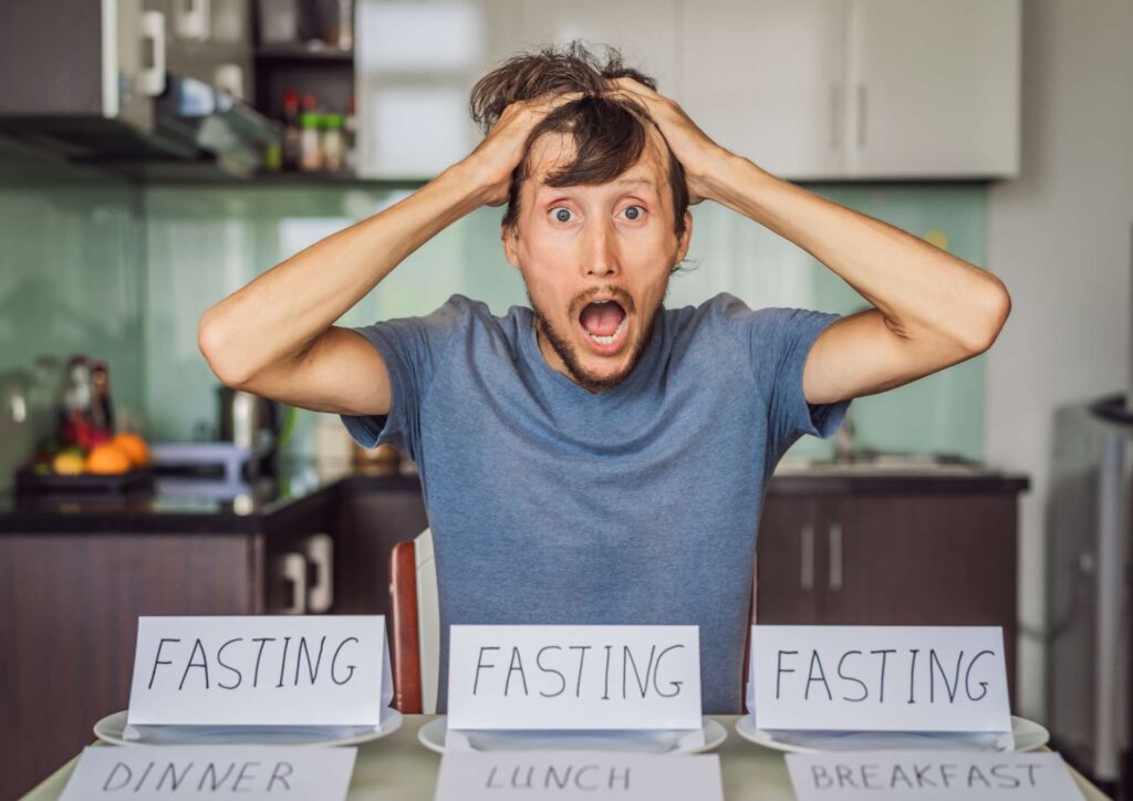Intermittent Fasting for Weight Loss: Does It Actually Work? 2 A man sits at a table with a sign displaying the words "fasting," "lunch," "dinner," and "breakfast."