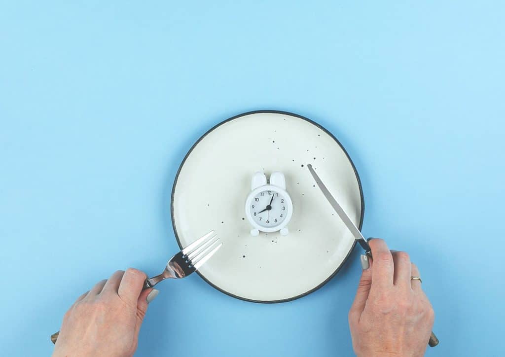 Intermittent Fasting for Weight Loss: Does It Actually Work? 14 A hand grips a fork and knife over a plate that displays a clock, illustrating the relationship between time and meals.