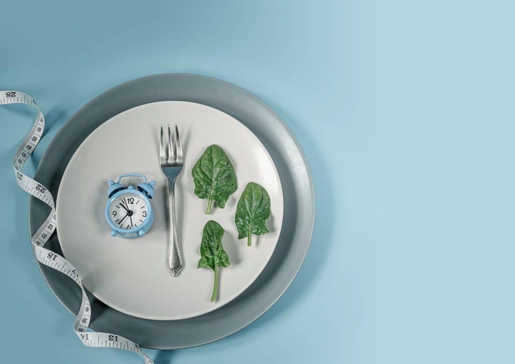 Intermittent Fasting for Weight Loss: Does It Actually Work? 16 A plate filled with spinach, a clock, and a measuring tape, representing nutrition and fitness tracking.