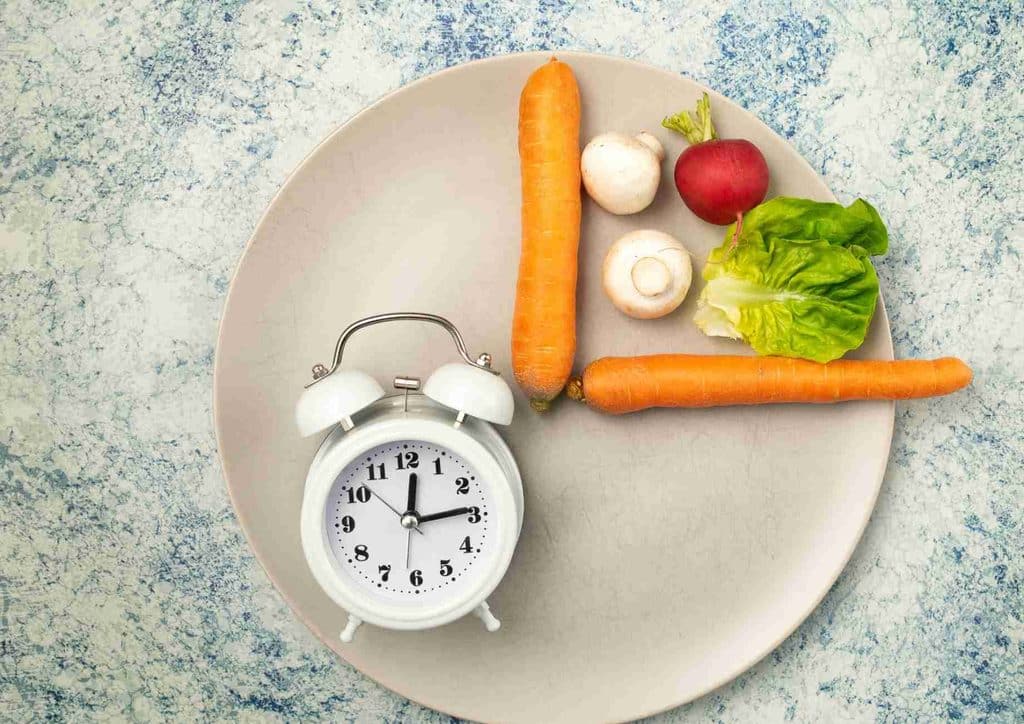 Intermittent Fasting for Weight Loss: Does It Actually Work? 23 A vibrant assortment of vegetables arranged on a plate beside an alarm clock, representing the importance of meal timing.