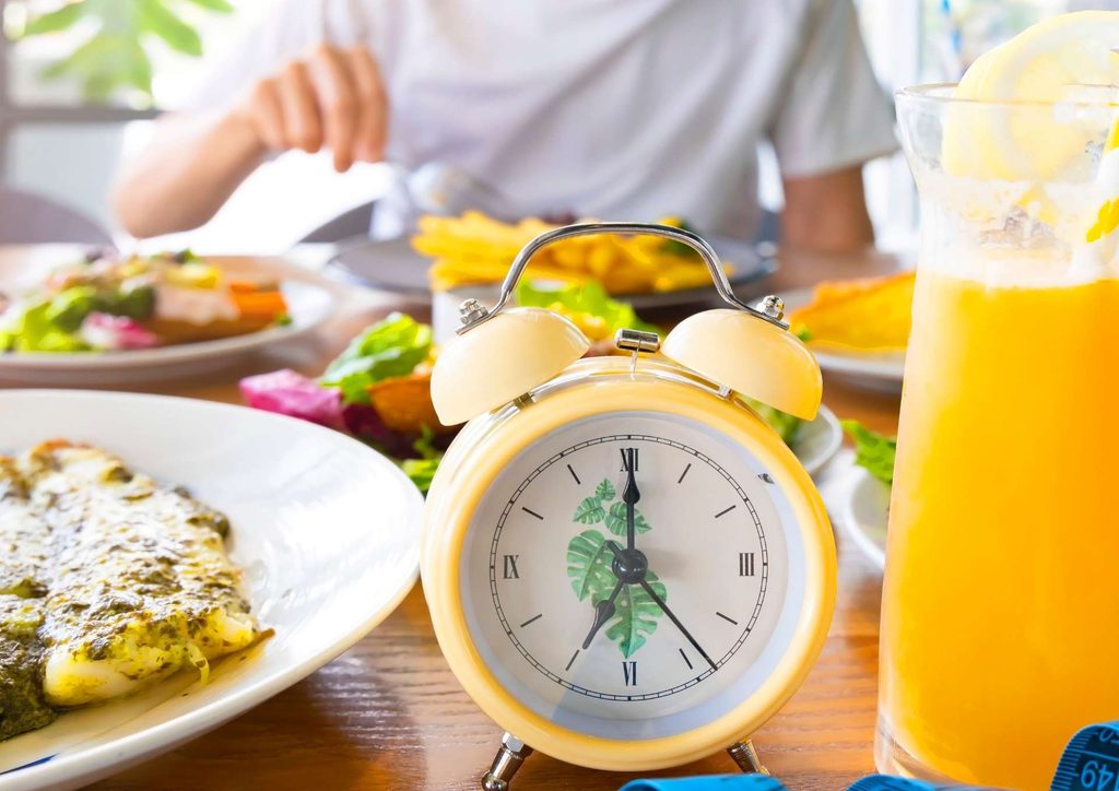 Intermittent Fasting for Weight Loss: Does It Actually Work? 18 A table set with various dishes and an alarm clock, indicating mealtime or a scheduled event.