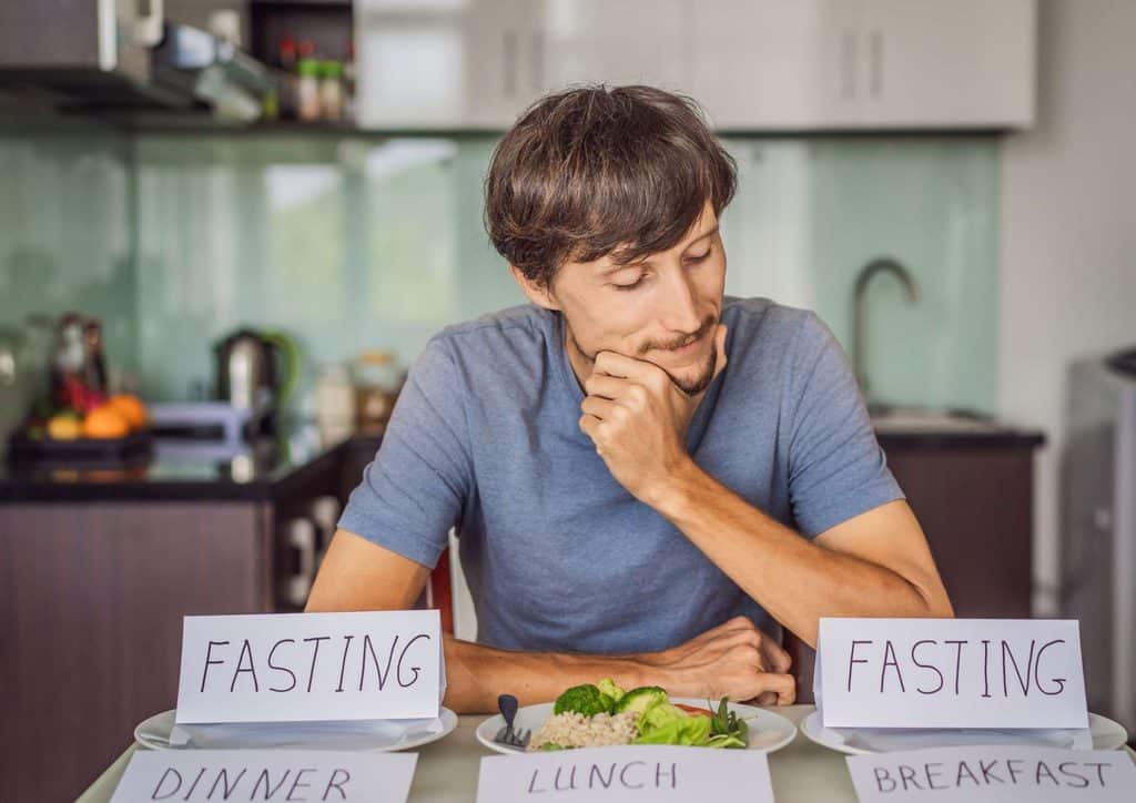Intermittent Fasting for Weight Loss: Does It Actually Work? 20 A man sits at a table with two plates labeled "fasting" and "eating," contemplating his meal choices.