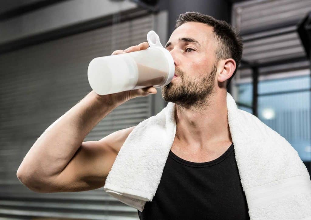 How to Speed Up Your Metabolism (What Actually Works) 11 A man holding a protein shake, drinking from it while standing in a gym setting.