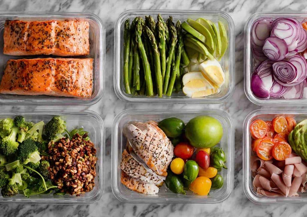Why Am I Not Losing Weight? 8 Reasons a Nutritionist Sees Every Week 28 A cutting board displaying sliced avocado, salmon, assorted nuts, and a bottle of oil, arranged for meal preparation.