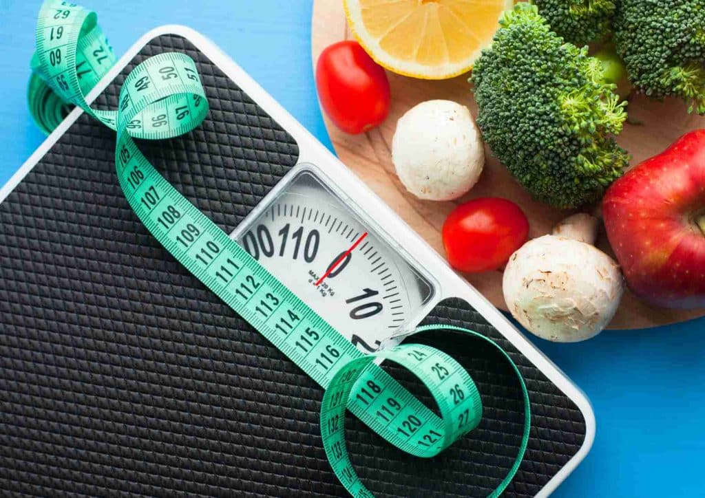 Why Am I Not Losing Weight? 8 Reasons a Nutritionist Sees Every Week 22 A scale surrounded by a tape measure and various fresh vegetables, symbolising health and nutrition.