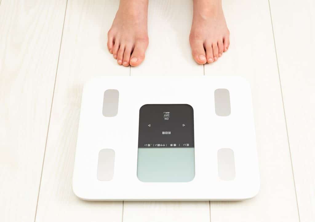 Why Am I Not Losing Weight? 8 Reasons a Nutritionist Sees Every Week 21 A person stands on a bathroom scale, measuring their weight in a home setting.