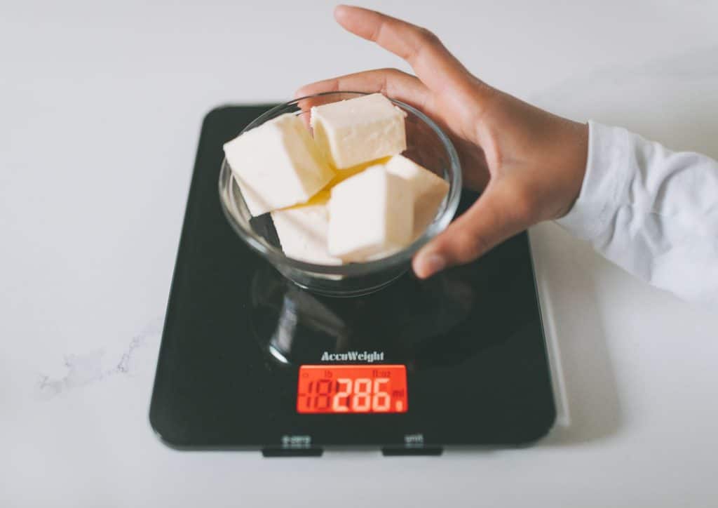 Not Losing Weight in a Calorie Deficit? Here's Why 7 A person weighing a piece of butter on a digital scale, focusing on the measurement display.
