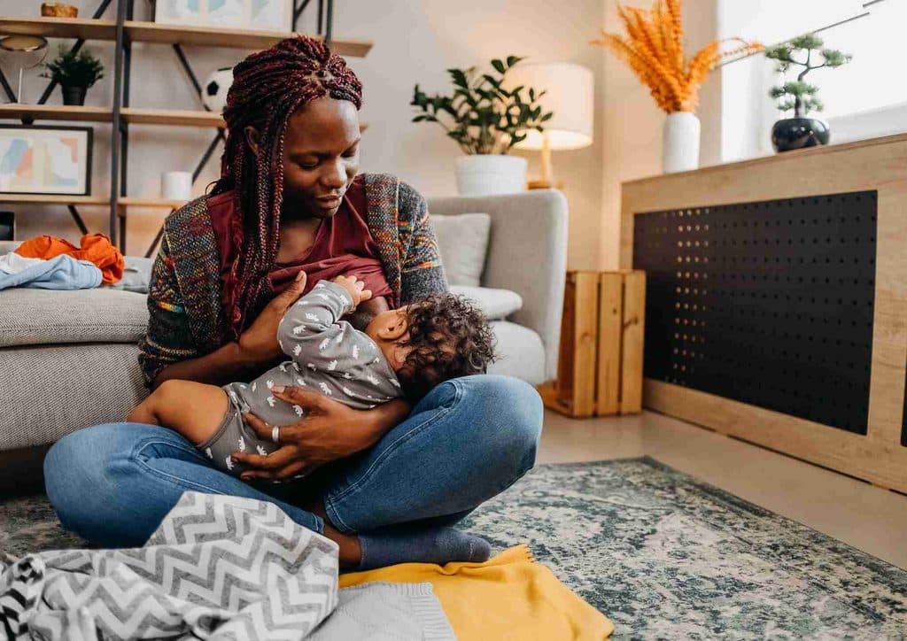 Losing Weight While Breastfeeding: What's Safe and Realistic 77 A woman sits in a living room, breastfeeding her baby while surrounded by cozy furniture and soft lighting.