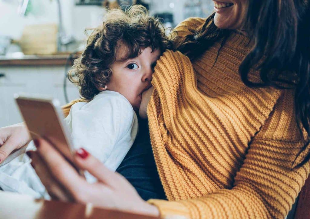 Losing Weight While Breastfeeding: What's Safe and Realistic 53 A woman holds a child in her arms while intently looking at her cell phone.