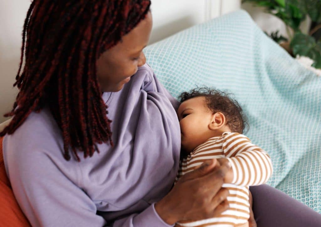 Losing Weight While Breastfeeding: What's Safe and Realistic 2 A woman seated on a couch, gently holding a baby in her arms, both appearing relaxed and content.