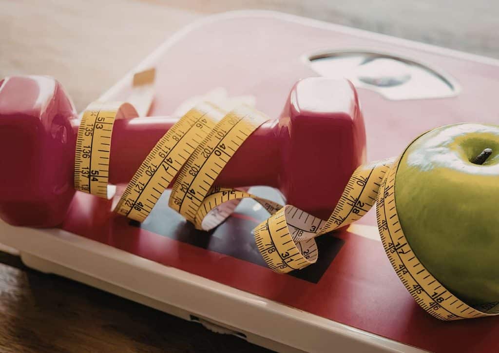 What Is a Balanced Diet for Weight Loss? 11 A red apple placed on a scale next to a measuring tape, indicating a focus on weight and measurement.