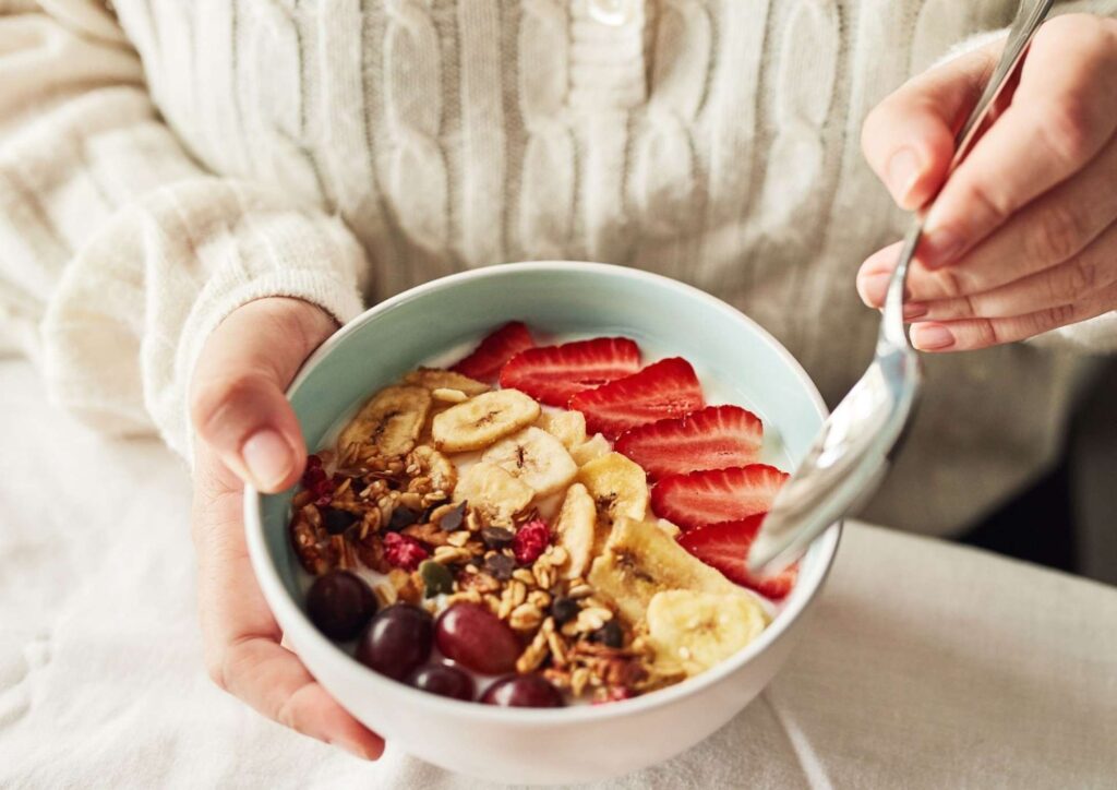 High Fibre Diet for Weight Loss: Why Fibre Keeps You Full 51 A woman holds a bowl of cereal topped with fresh fruit and nuts, smiling as she prepares to enjoy her meal.