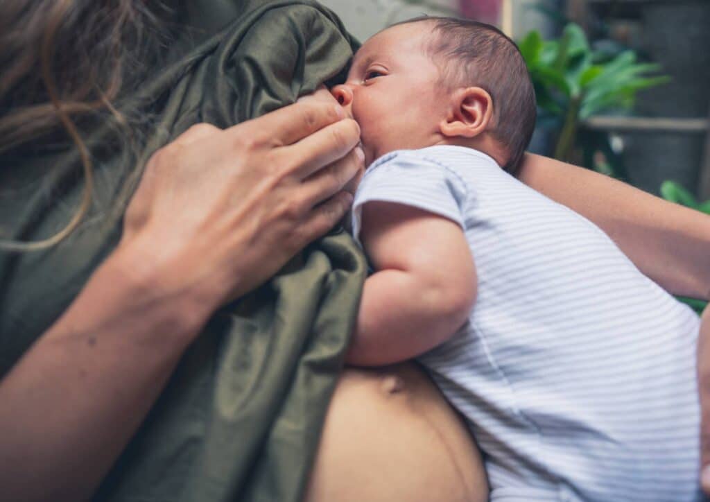 Losing Weight While Breastfeeding: What's Safe and Realistic 54 A woman sits on a bed, breastfeeding her baby, creating a nurturing and intimate atmosphere.