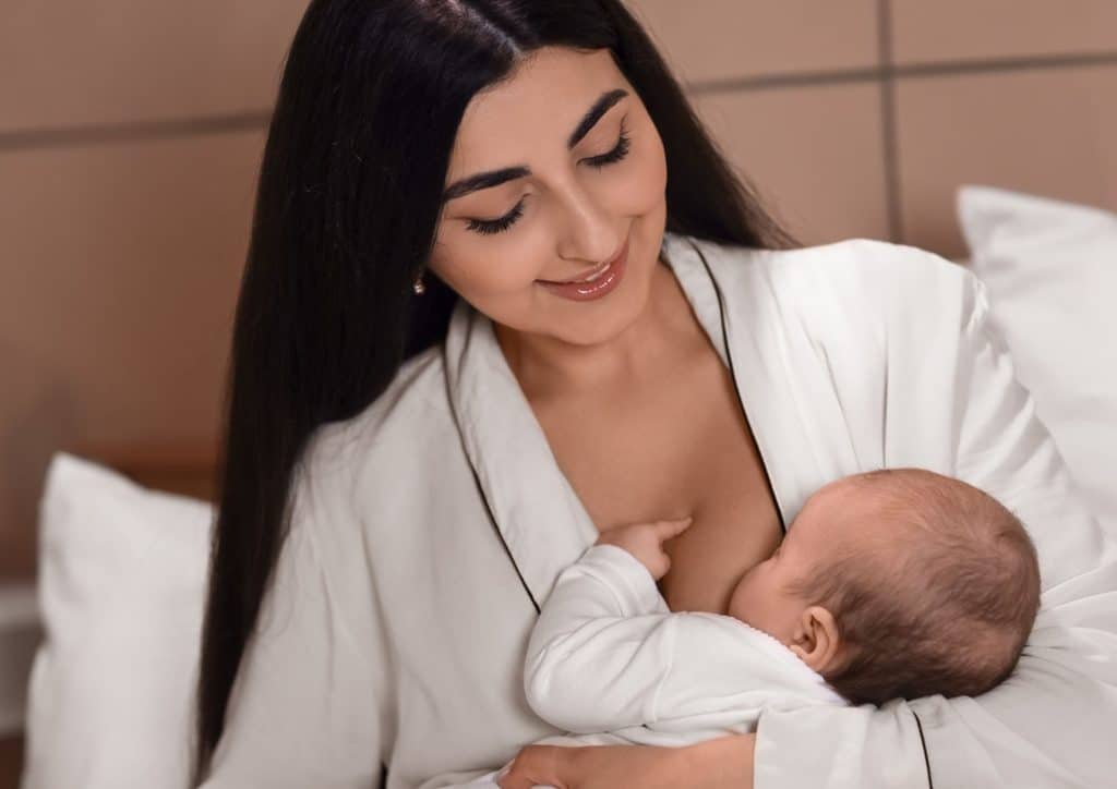 Losing Weight While Breastfeeding: What's Safe and Realistic 57 A woman breastfeeding her baby while sitting in bed, creating a nurturing and intimate atmosphere.