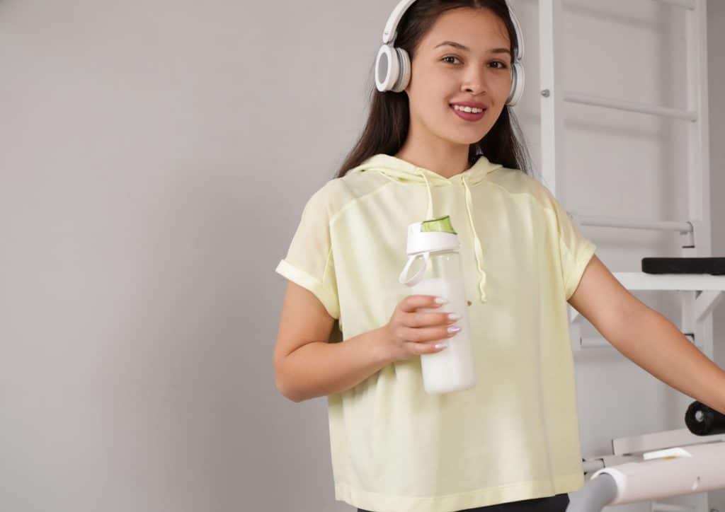 Is Whey Protein Good for Weight Loss? 52 Asian woman wearing headphones, smiling while holding a bottle of water, suggesting hydration and enjoyment.