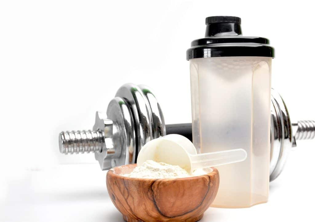 Is Whey Protein Good for Weight Loss? 54 A bottle of protein powder placed beside a dumbbell on a flat surface, suggesting fitness and nutrition.