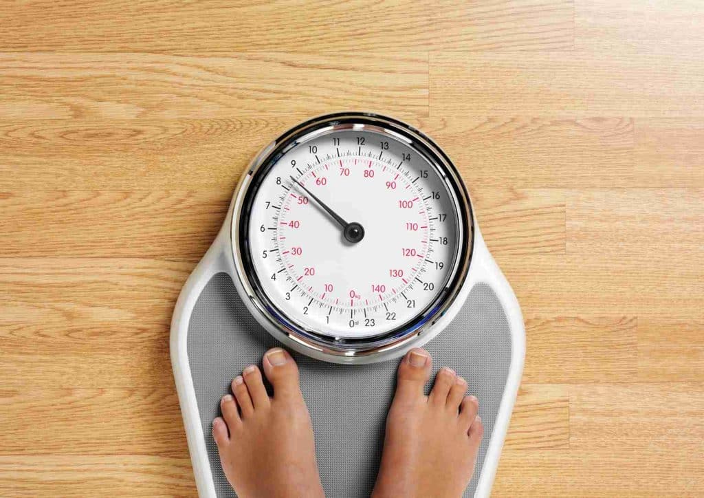 What Is a Balanced Diet for Weight Loss? 16 A person stands on a scale, feet firmly on the floor, measuring their weight.
