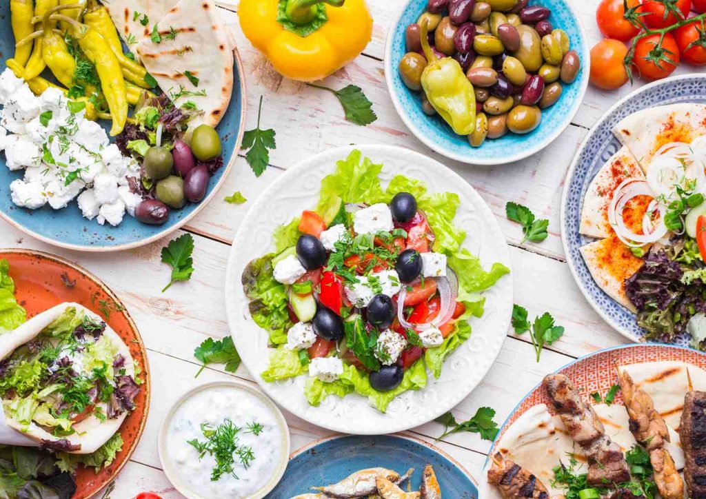 Is the Mediterranean Diet Good for Weight Loss? 12 A selection of Greek dishes on plates, including moussaka, tzatziki, olives, and stuffed grape leaves.