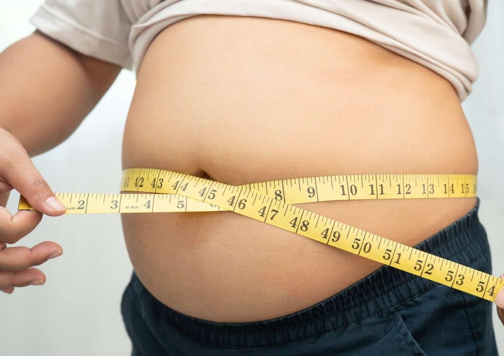 Postpartum Weight Loss: A Gentle, Realistic Guide 7 A woman measures his waist with a tape measure, focusing on his stomach area in a well-lit room.