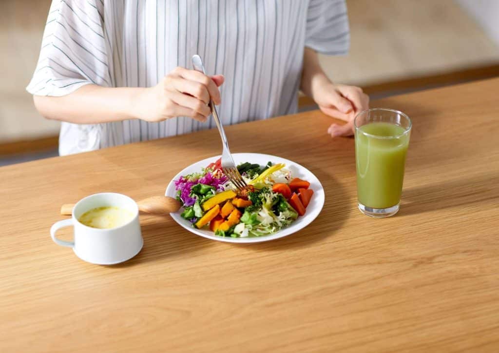 Easy Meals for Weight Loss When You're Short on Time 49 A woman enjoys a fresh salad while sipping a glass of juice, seated at a table.