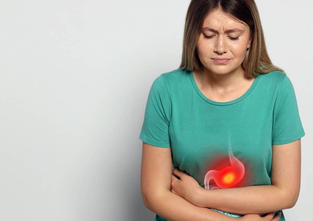 High Fibre Diet for Weight Loss: Why Fibre Keeps You Full 30 A woman sitting on a couch, holding her stomach in discomfort, indicating abdominal pain.