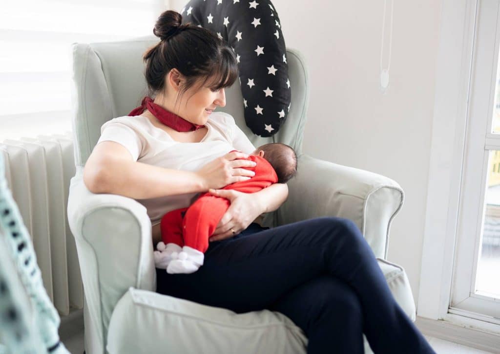 Losing Weight While Breastfeeding: What's Safe and Realistic 22 A woman sits in a chair, breastfeeding her baby, creating a nurturing and intimate moment between mother and child.