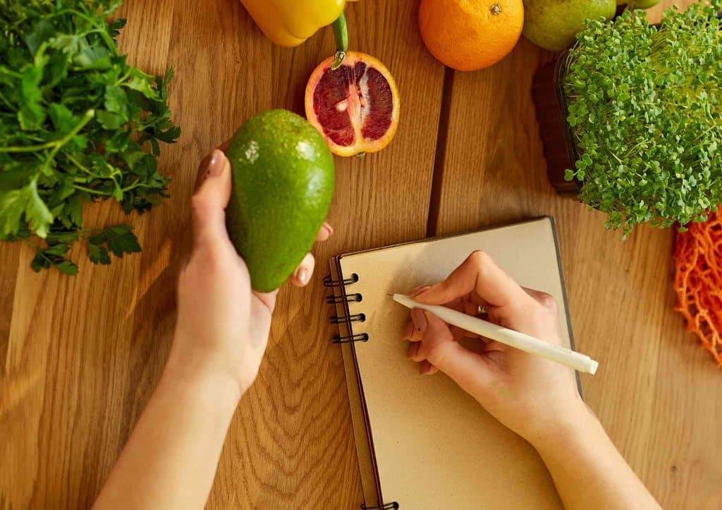 Healthy Meal Plans for Weight Loss: How to Build One That Lasts 15 A person writes in a notebook with a pen, surrounded by a variety of fresh vegetables on a table.