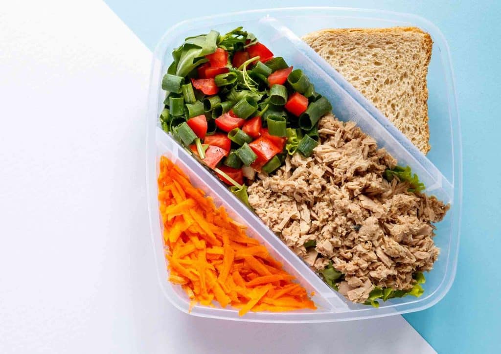 Healthy Lunches for Weight Loss: Work and Home Ideas 43 A plastic container filled with tuna salad, accompanied by sliced carrots and a piece of bread on the side.