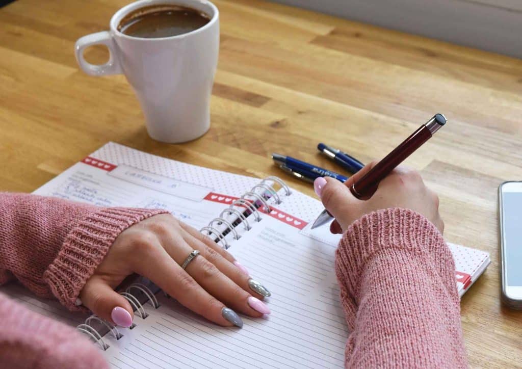 Healthy Meal Plans for Weight Loss: How to Build One That Lasts 20 A woman seated at a table, writing in a notebook with a pen, focused on her task.