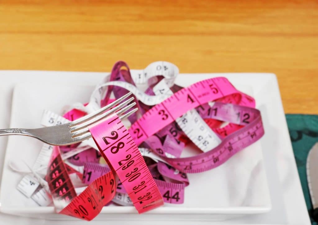 Easy Meals for Weight Loss When You're Short on Time 41 A plate with a fork and a measuring tape arranged on top, symbolising portion control and dietary measurement.