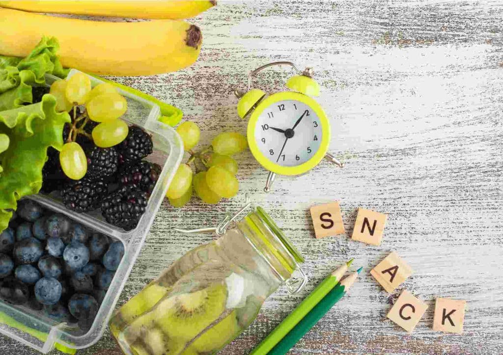 Healthy Snacks for Weight Loss That Actually Keep You Full 23 A container filled with assorted fruits and vegetables, accompanied by a clock and a pencil on a wooden surface.