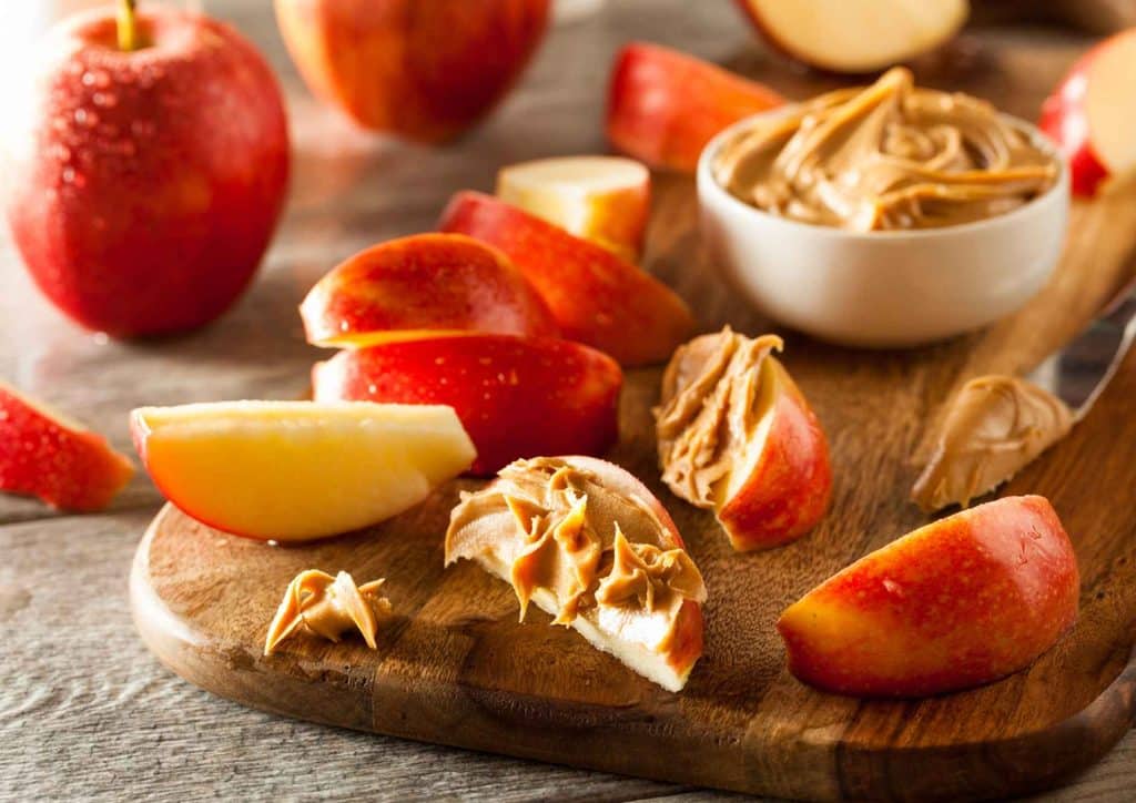 Healthy Snacks for Weight Loss That Actually Keep You Full 21 Sliced apples arranged on a cutting board with a small bowl of peanut butter beside them.
