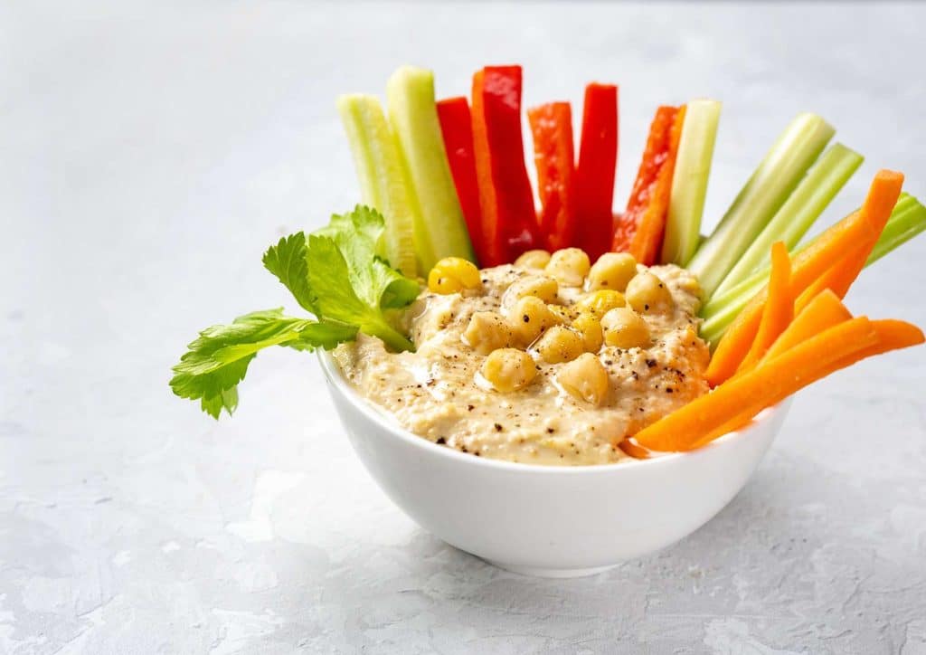 Healthy Snacks for Weight Loss That Actually Keep You Full 3 A bowl of hummus surrounded by fresh carrot sticks, celery, and cucumber slices for dipping.