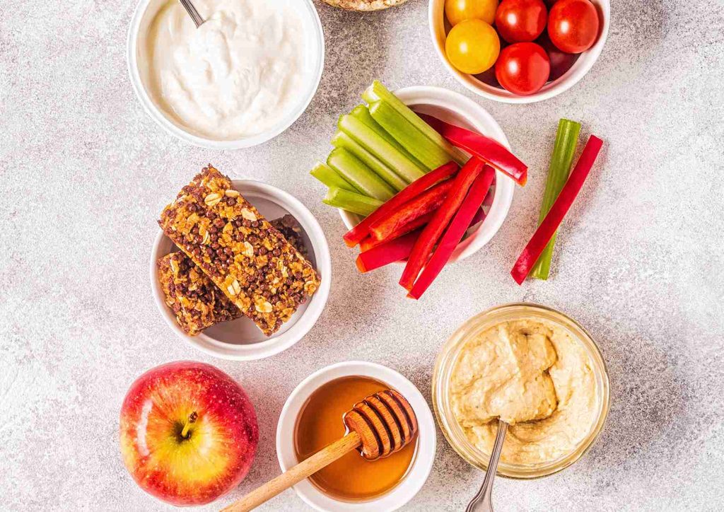 Healthy Snacks for Weight Loss That Actually Keep You Full 5 A selection of nutritious snacks including fresh apples, celery sticks, carrot sticks, and a serving of hummus.