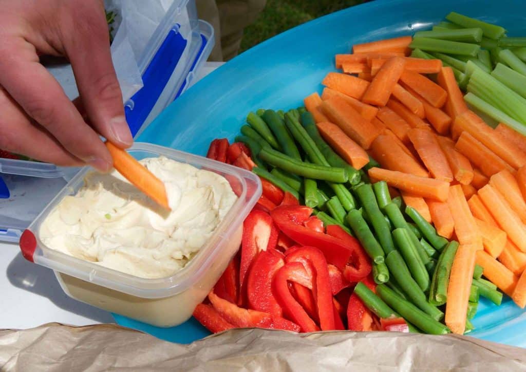 Healthy Snacks for Weight Loss That Actually Keep You Full 6 A person dips fresh carrot sticks into a bowl of creamy dip, showcasing a healthy snack option.