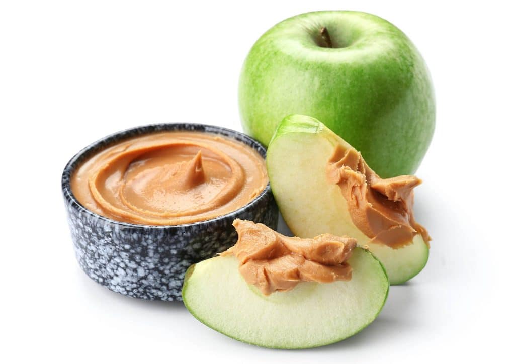 Healthy Snacks for Weight Loss That Actually Keep You Full 8 A jar of peanut butter next to a sliced apple on a white background, showcasing a healthy snack combination.