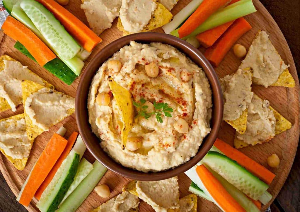 Healthy Snacks for Weight Loss That Actually Keep You Full 11 A plate of creamy hummus surrounded by fresh vegetables and crunchy crackers, arranged for a healthy snack.
