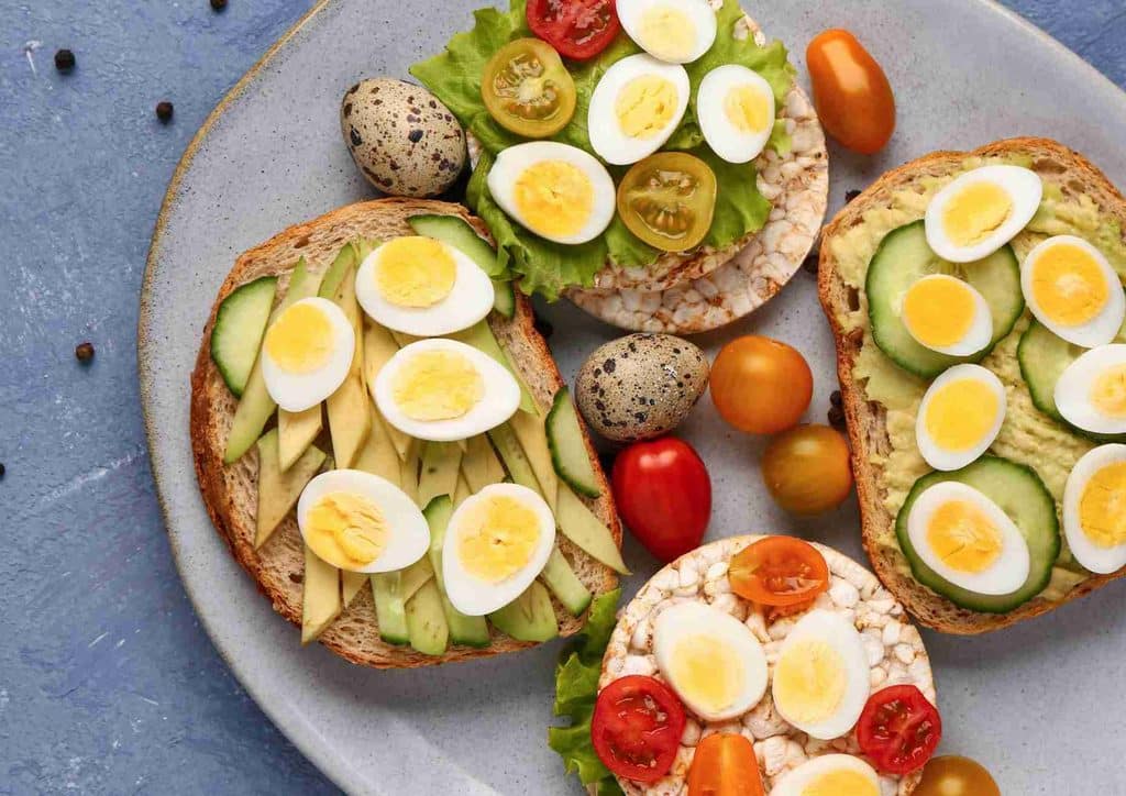 Easy Meals for Weight Loss When You're Short on Time 36 A slice of toast topped with eggs, sliced tomatoes, and avocado, arranged attractively on a white plate.